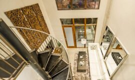Loft apartment with long comfortable couch, modern wooden console and coffee table, and metal spiral staircase.