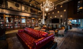 Clubroom with plush double sided couch, rich wood floors with rugs, and glowing chandeliers.