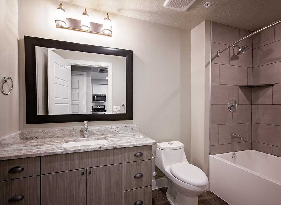 Bathroom with smooth stone countertops, tiled shower and rich wood floors.