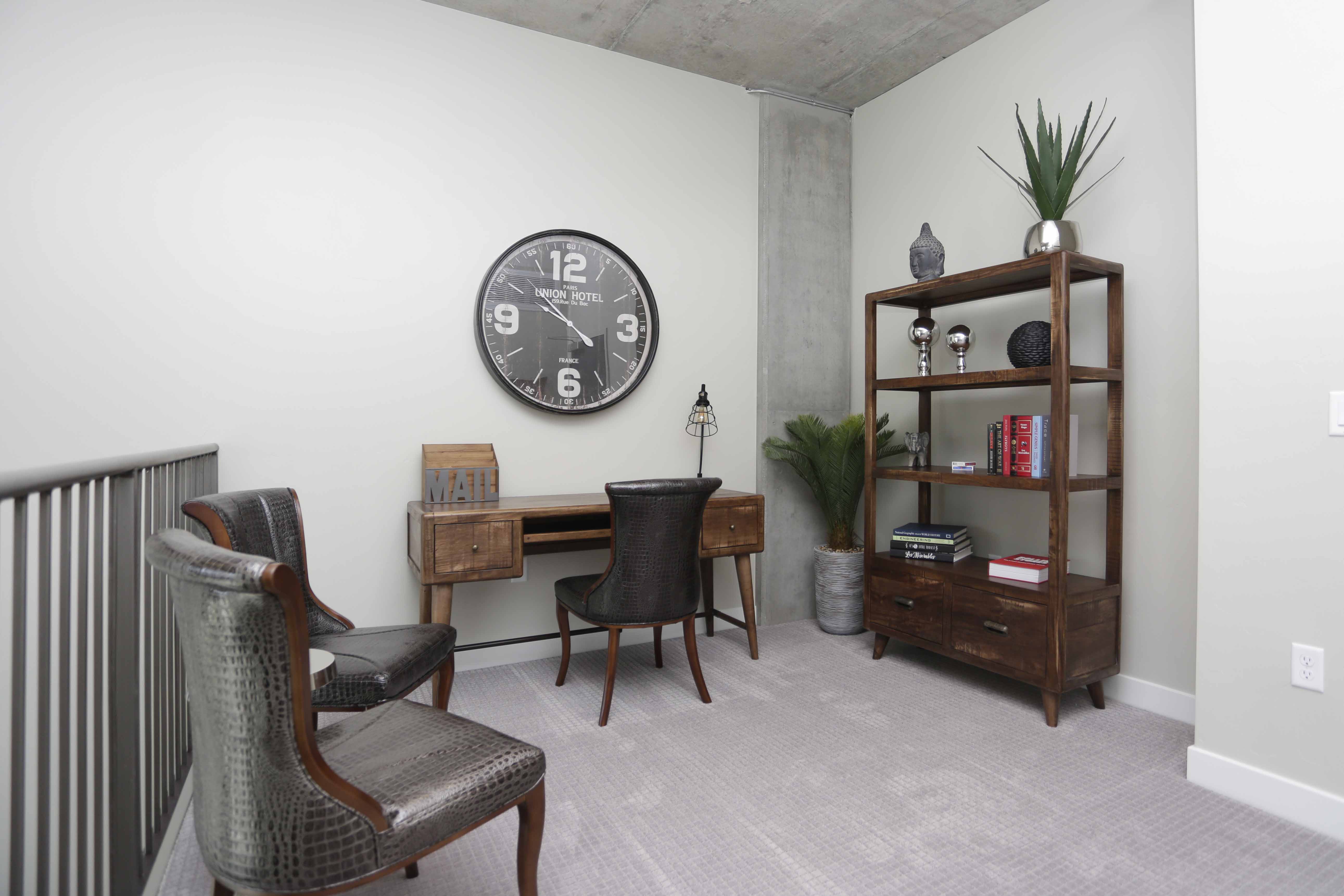 Living space with vintage wood desk, leather chairs, bookshelf with plants, and large wall clock.