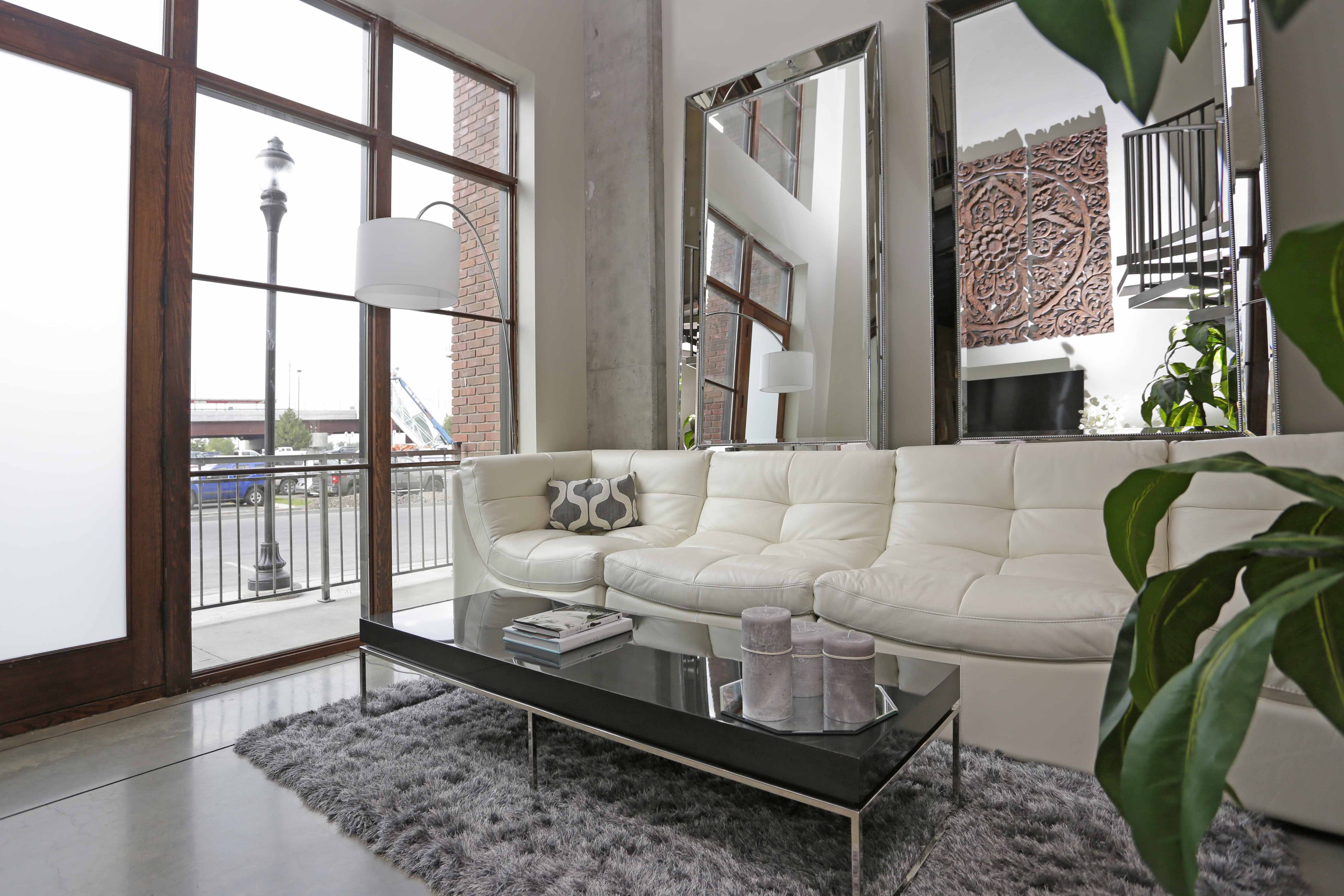Loft apartment with long couch, tall decorative mirrors, and front door opening to sidewalk.