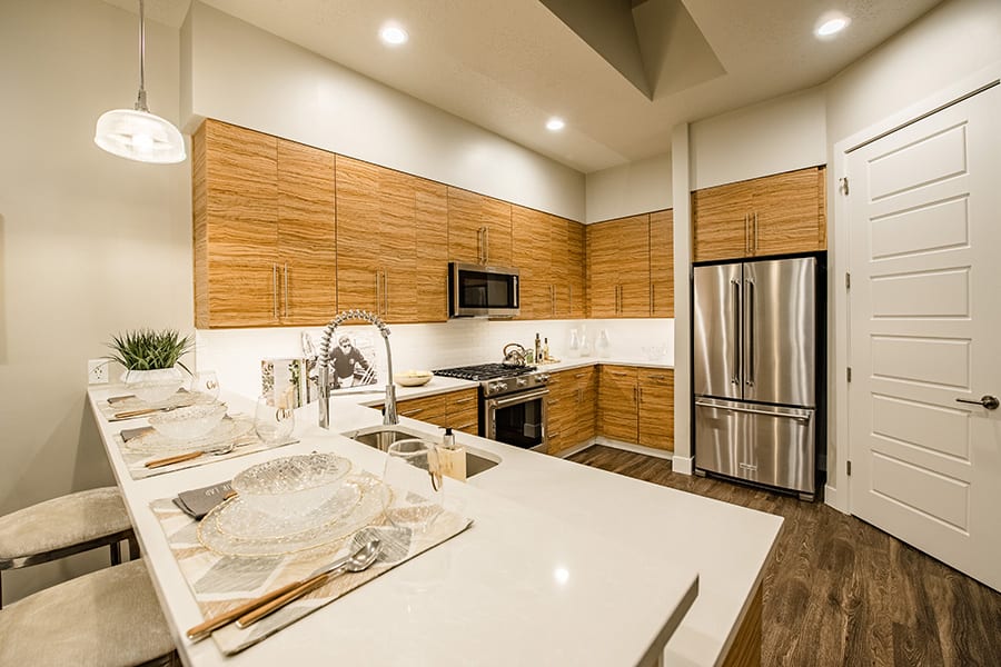 Kitchen with wood cabinets and floors, smooth countertops, and large french door stainless steel refrigerator.