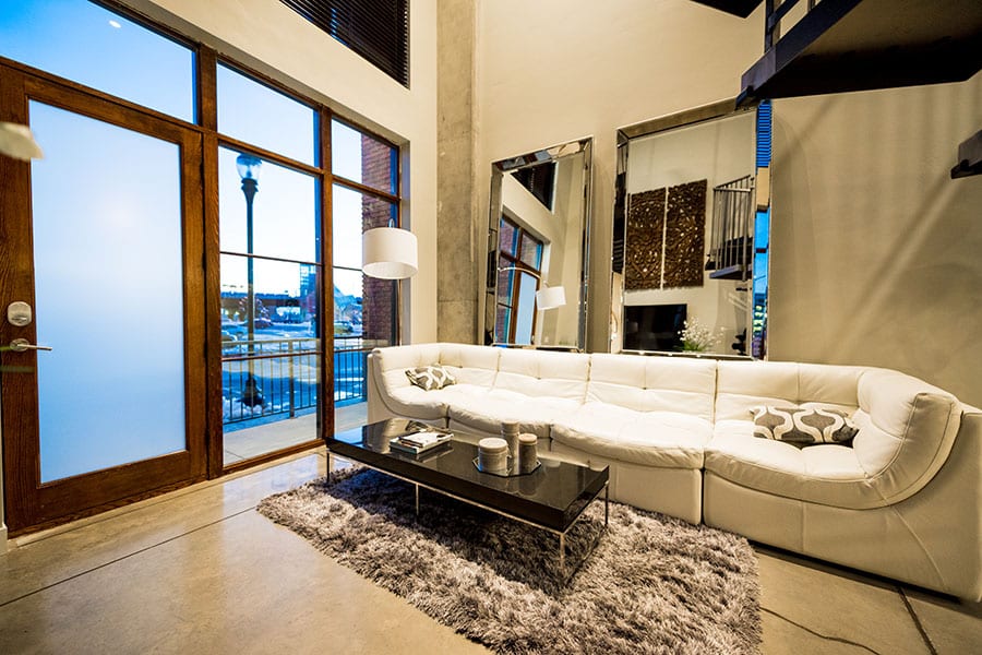 Loft apartment with long couch, plush rug, tall decorative mirrors, and polished concrete floors.