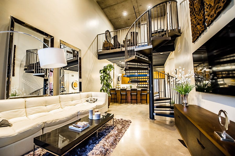 Loft apartment with long comfortable couch, modern wooden console and coffee table, and metal spiral staircase.