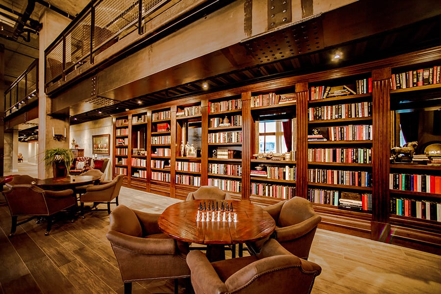 Clubroom with large bookshelf wall and a round wood table with chess set.