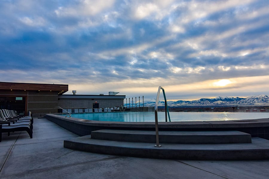 Rooftop swimming pool deck under cloudy skies looking towards the sun and mountains.