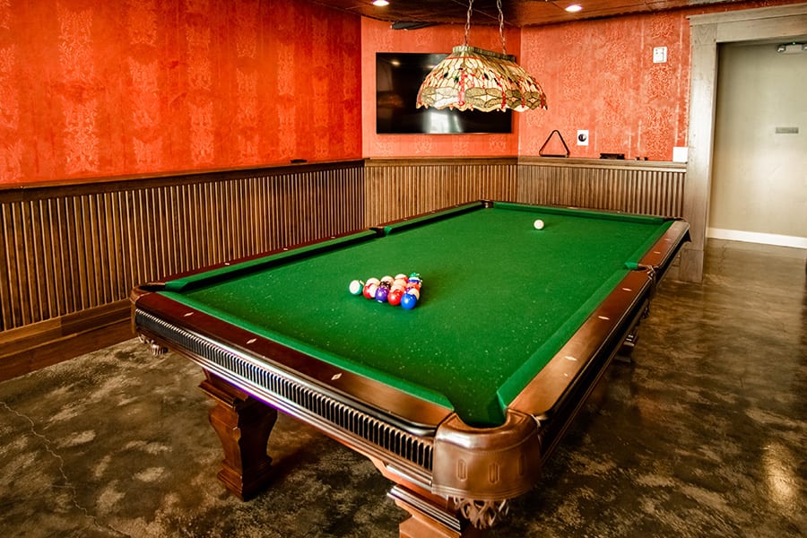 Game room with polished concrete floors, wood panels, and large pool table with lamp.