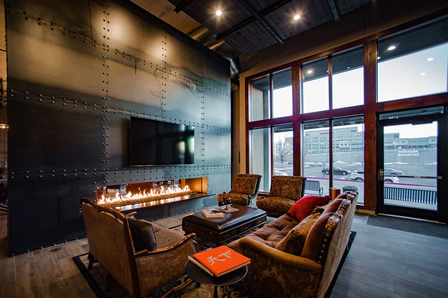 Clubroom space with large windows, plush couches, and a large TV mounted on a riveted metal wall.