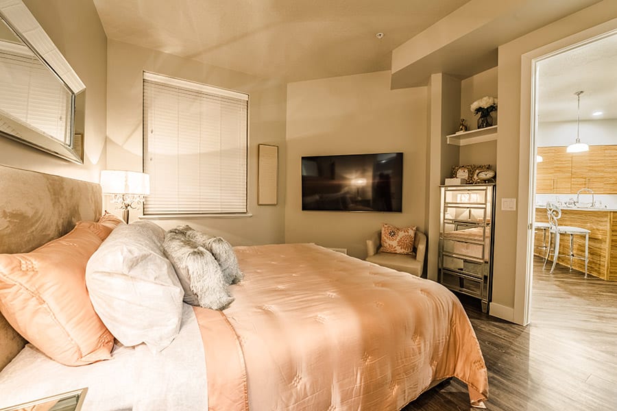 Warm bedroom with large bed, reflective dresser, large televsion, and a plush leather chair.