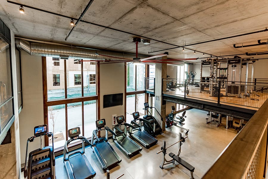Fitness center from second story looking down on treadmills and stair steppers with large floor to ceiling windows.