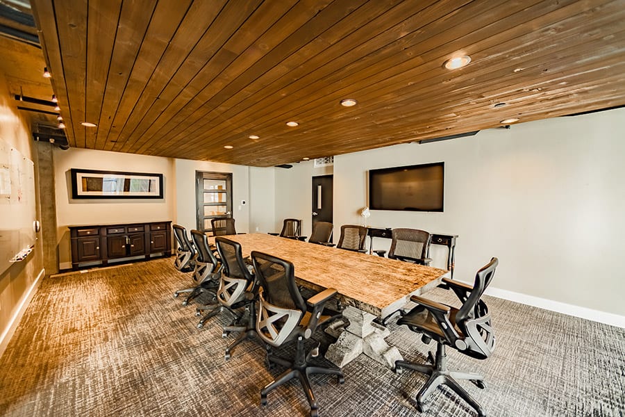 Conference room with large stone table, carpeted floors, and rich wood ceiling with recessed lights.