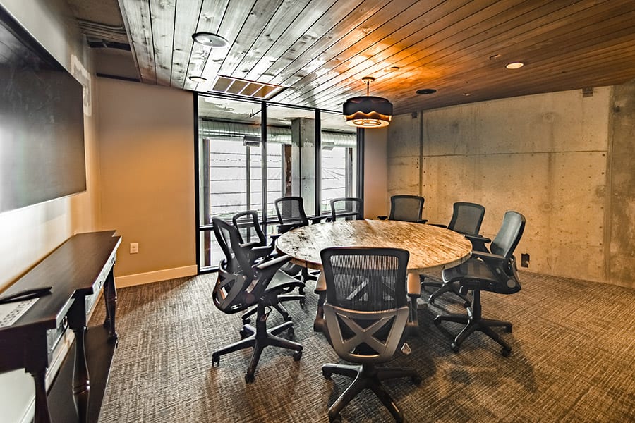 Conference room with circular stone table, concrete walls, and rich wood ceiling.