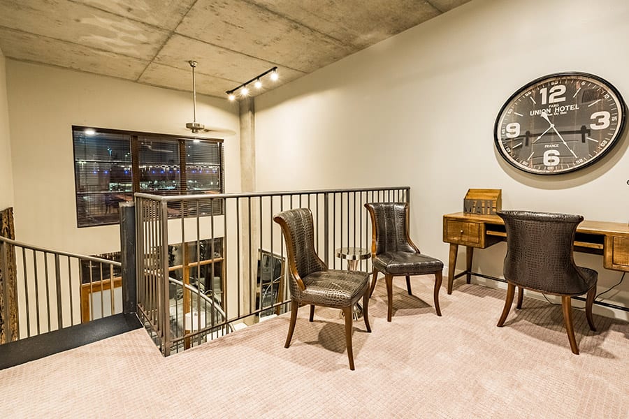 Second story of loft apartment with vintage wooden desk, leather chairs and metal spiral staircase.