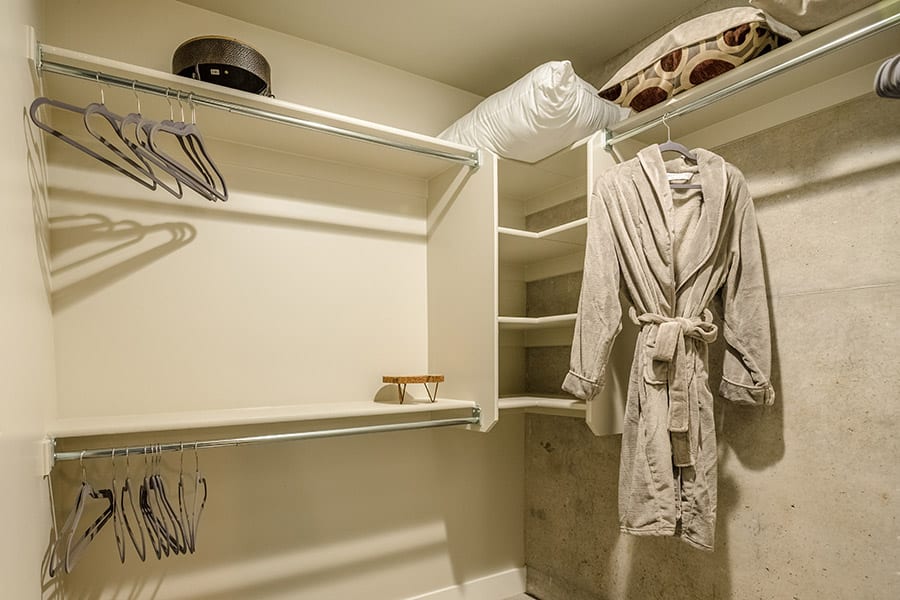 Walk in closet corner with clothing rods, shelves, stored bedding and a robe.
