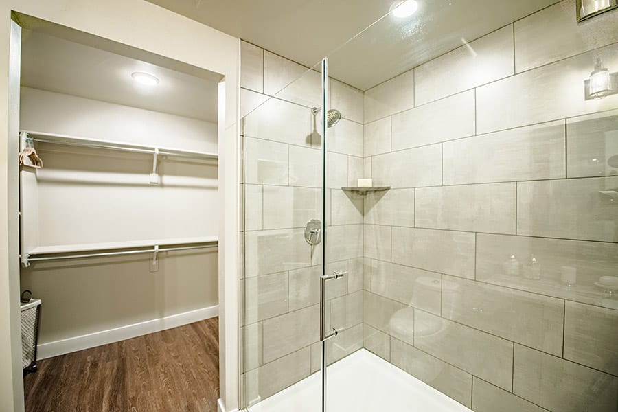 Bathroom with large tiled shower, sliding glass doors, and wood floors opening to walk in closet.