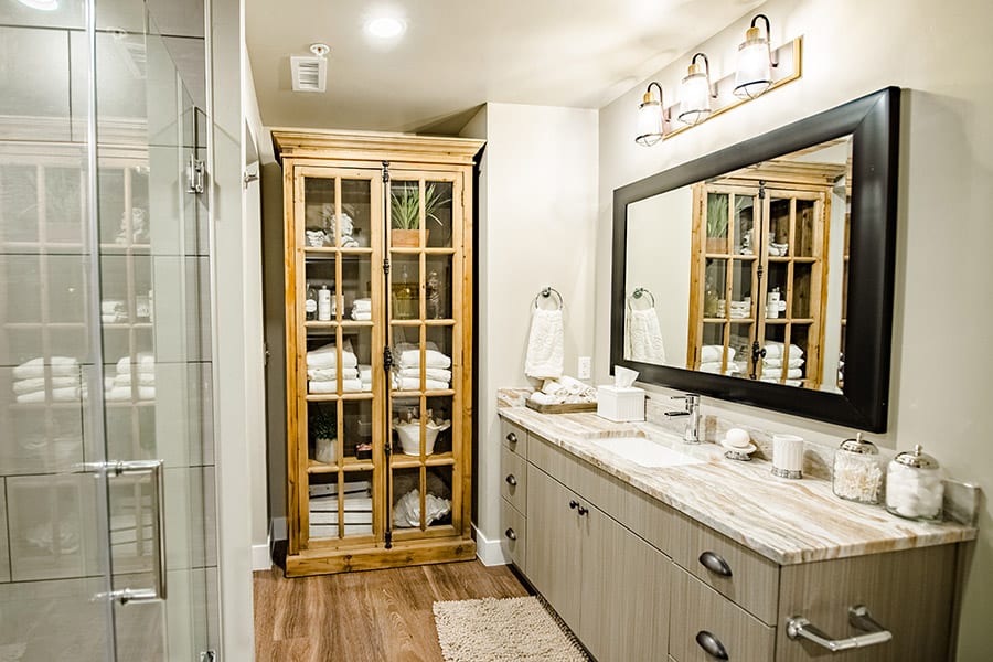 Bathroom with wood floors, glass shower doors, and large wood cabinet with linens and decorations.